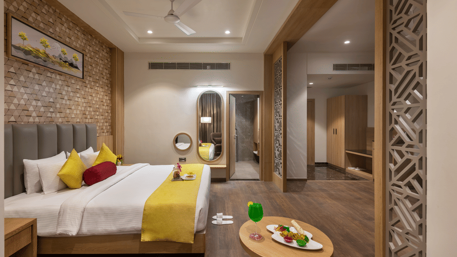 A spacious and elegantly designed suite at Lords Inn Somnath, featuring a king-size bed with plush pillows, modern decor, and a table set with refreshments.