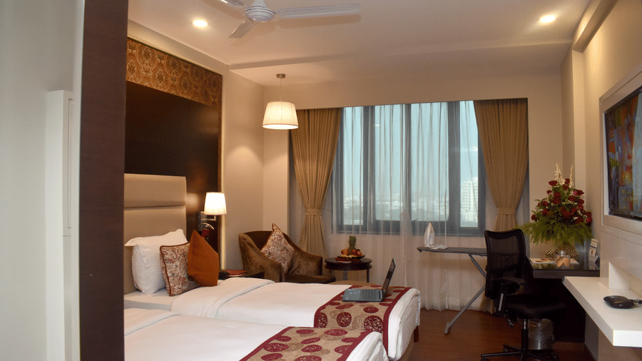 A hotel room with twin beds, work desk and comfortable seating near a large window at Lords Plaza Surat.