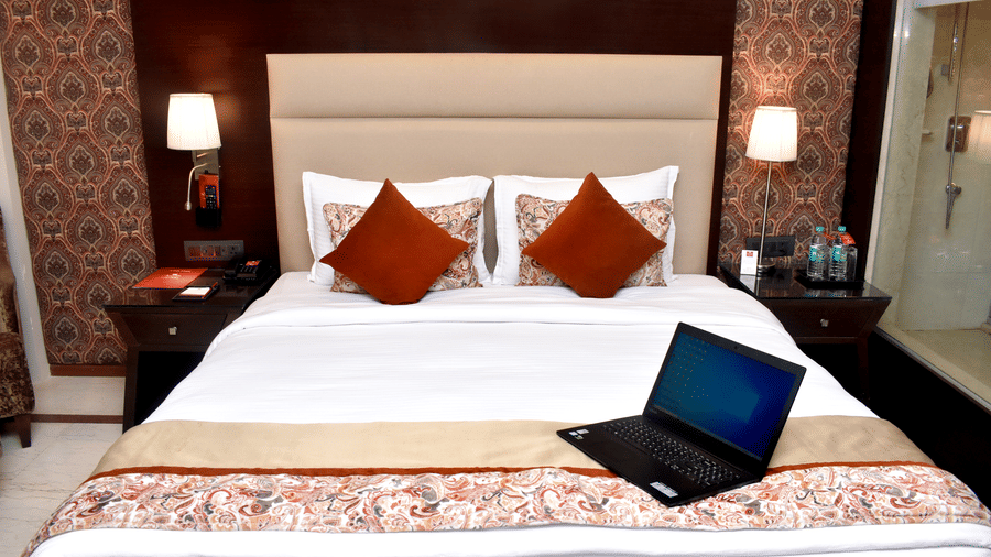 A bedroom in Lords Plaza Surat featuring a double bed decked with plush pillows, patterned runner, an open laptop and a large head-rest highlighting its modern interiors