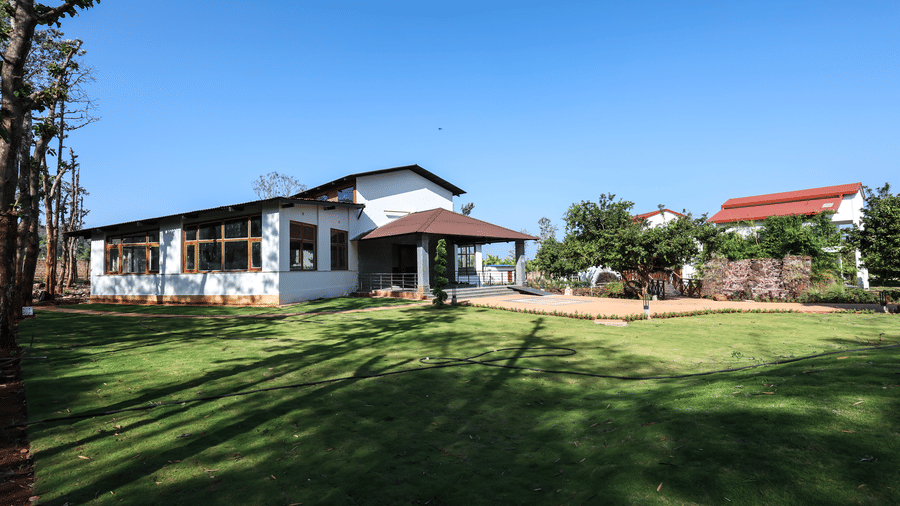 A white resort villa situated beside a wide green lawn with shadows from trees cast across the grass | Lords Sahyadri Resort, Shivamogga