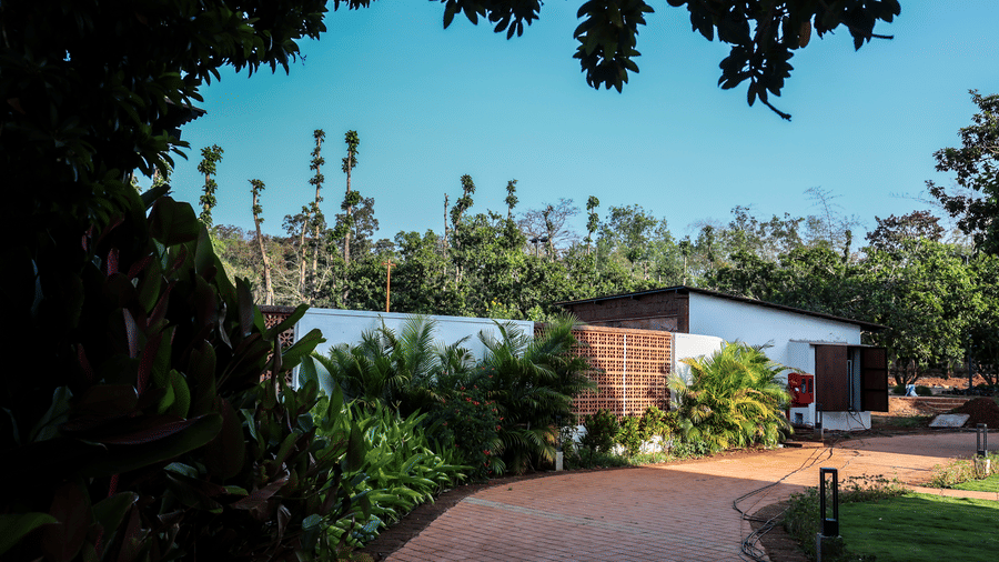 A paved stone pathway leading through lush green trees and plants towards a modern white villa | Lords Sahyadri Resort, Shivamogga