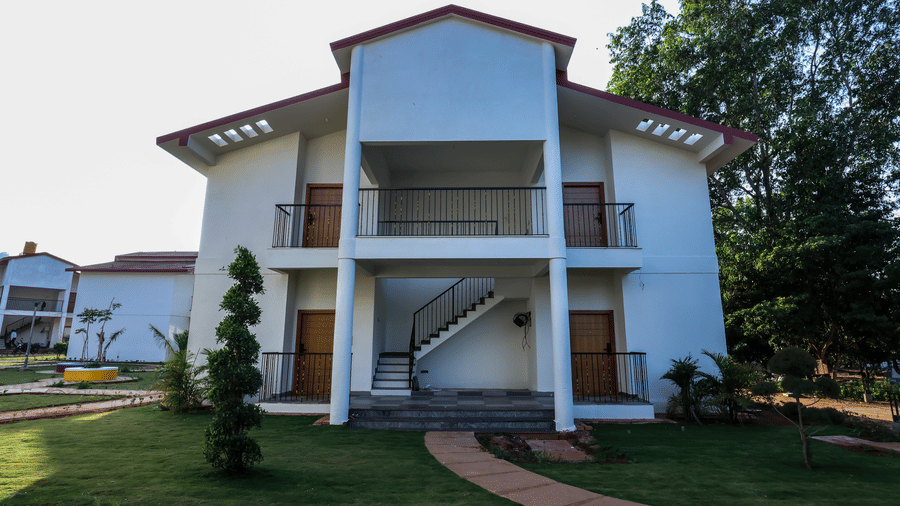 A front view of a two-storey white resort building with a red-trimmed roof, balconies, and a stone path on the lawn | Lords Sahyadri Resort, Shivamogga