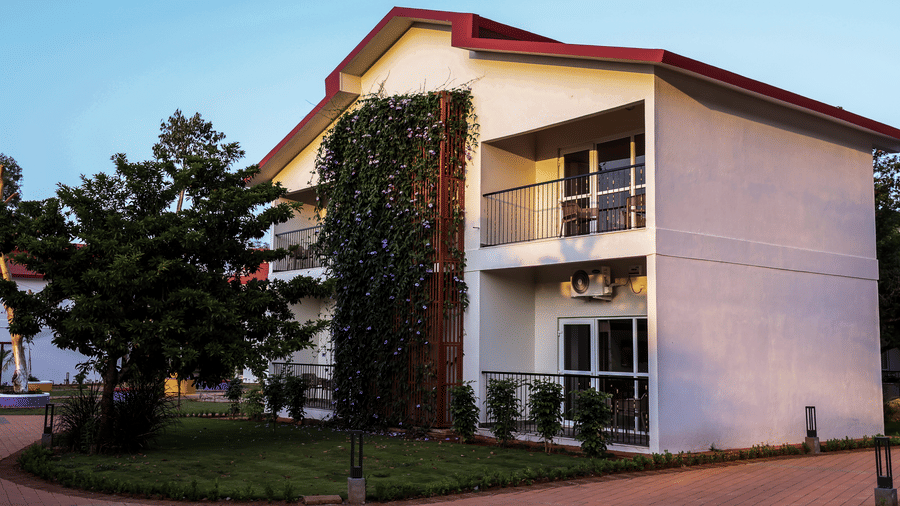 A 2-storey resort villa with climbing green vines on its wall, bordered by a brick pathway | Lords Sahyadri Resort, Shivamogga