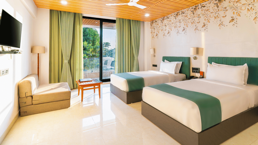 Bright twin bedroom at Lords SKD Resort, Salangpur, featuring teal accents, a sofa, and sliding doors leading to a balcony.