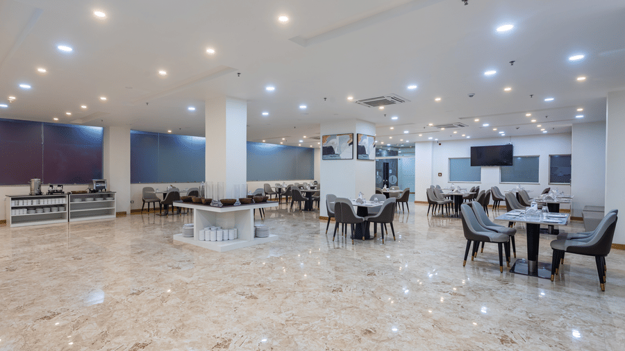 Corner view of the Blue Coriander Restaurant at Mandala Norling Lords Prime in Kathmandu with various seating arrangements, neatly placed cutlery and bright overhead lighting.