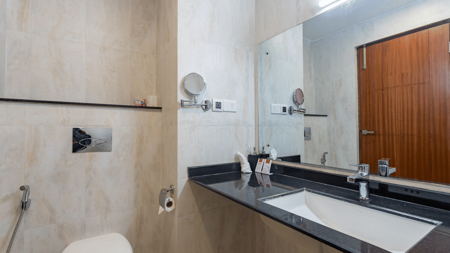 A toilet with sink, mirror and toiletries