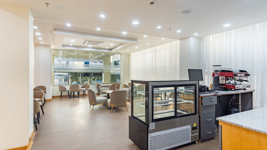 Entrance view of L Cafe at Mandala Norling Lords Prime Kathmandu showing the pastry cooler and seating under bright spotlights.