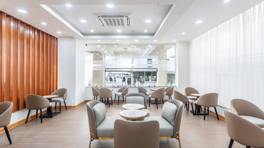 Dining area of L Cafe at Mandala Norling Lords Prime Kathmandu with cushioned chairs and large windows overlooking the view outside..