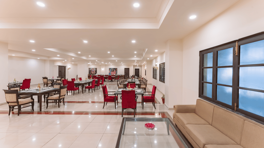 An indoor, well-lit, spacious dining area at the best restaurant in Nathdwara, Shri Vallabh Vilas Lords Plaza, featuring red chairs, tiled floor, and a seating lobby area with windows.