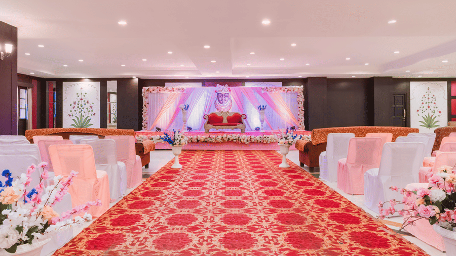 A decorated stage and aisle in the Raj Mahal banquet hall in Nathdwara at Shri Vallabh Vilas Lords Plaza, lined with chairs and floral arrangements.