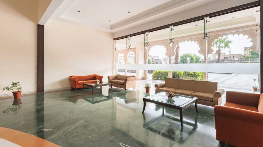 Spacious indoor seating area with orange sofas, glass tables, and large windows framing arched architecture outside at Shri Vallabh Vilas Lords Plaza Nathdwara.