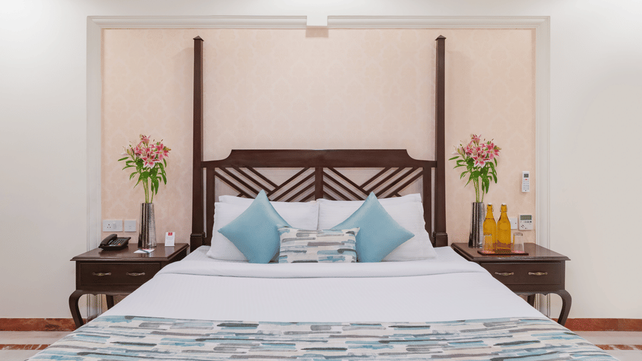 An elegant well lit premier suite at Shri Vallabh Vilas Lords Plaza Nathdwara, featuring a twin size bed, bedside tables and wooden furnishings.