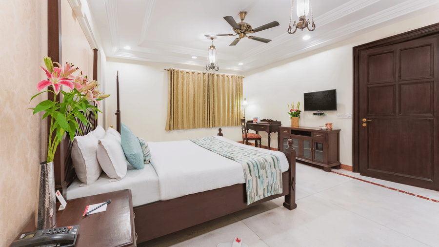 Elegant premier suite at Shri Vallabh Vilas Lords Plaza Nathdwara with a large bed, a T.V., fresh flowers, ceiling fan, and modern wooden furnishings.