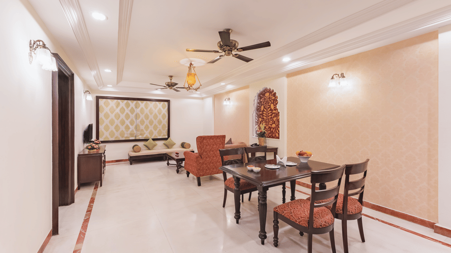 A well lit spacious living and dining area at Shri Vallabh Vilas Lords Plaza Nathdwara, featuring classic wooden furniture, warm-toned walls, ceiling fans, and a blend of traditional and contemporary decor.