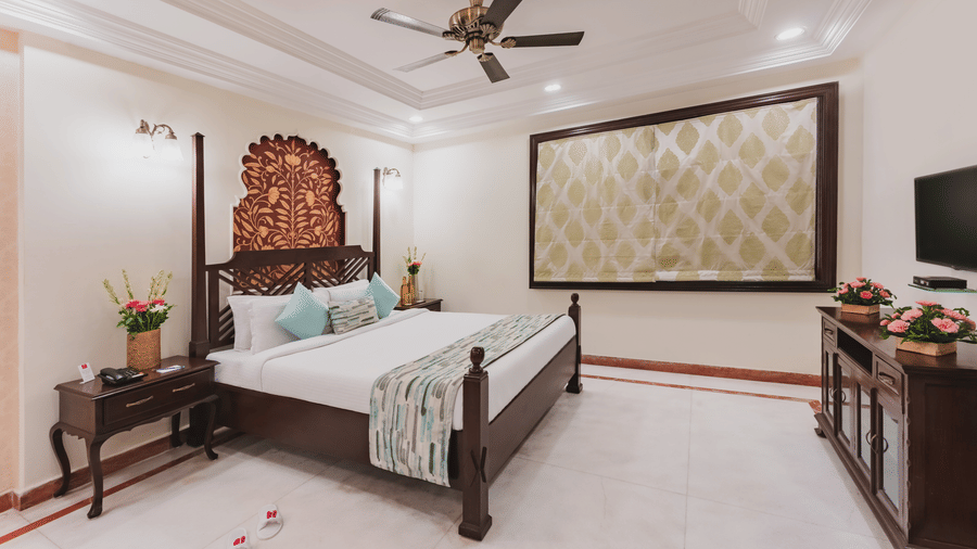 A bedroom featuring wall arts, pendant lights, a bedside table, ceiling fan and a T.V. above the cabinet at Shri Vallabh Vilas Lords Plaza Nathedwara.