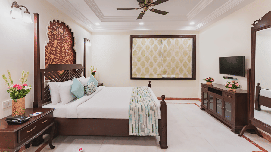 A view of the room featuring a twin size bed with wooden architect furnishings, a ceiling fan, wall arts and bedside table, a T.V. and a mirror at Shri Vallabh Vilas Lords Plaza Nathdwara.