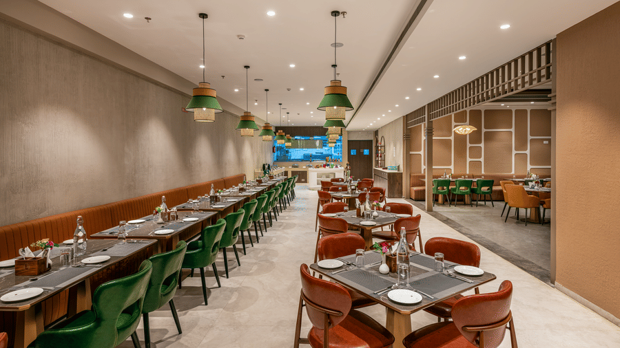 A vibrant restaurant scene featuring emerald green seating, a long banquet table, and unique woven light fixtures reflecting in large wall mirrors - Skkylight Lords Inn, Nanded