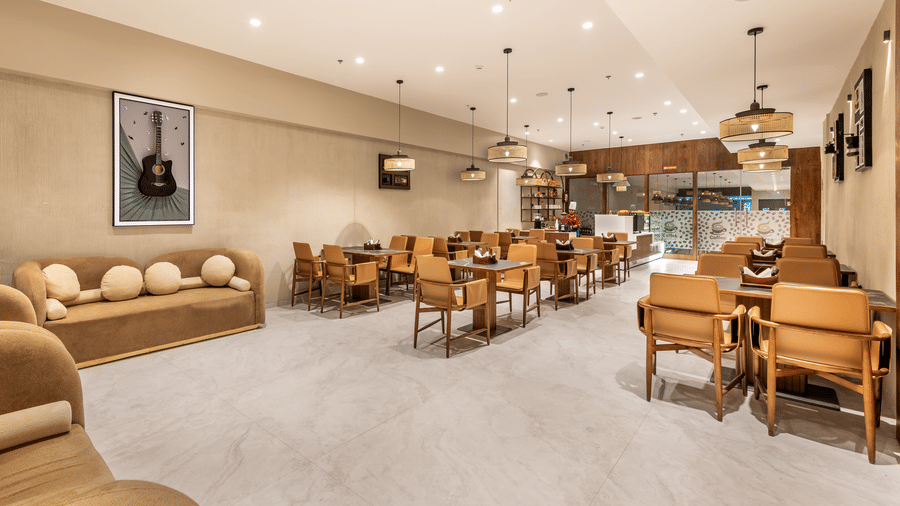 A wide-angle shot of the L Café dining area featuring contemporary mustard-yellow arm chairs, wooden tables, and a bright, airy atmosphere – Skkylight Lords Inn, Nanded