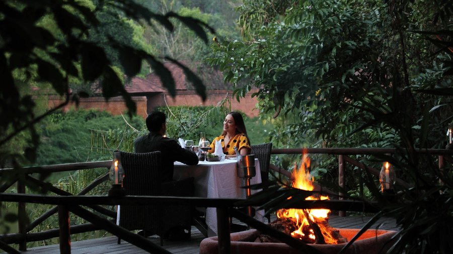 Couple dining on a wooden deck with bonfire at Evolve Back Coorg