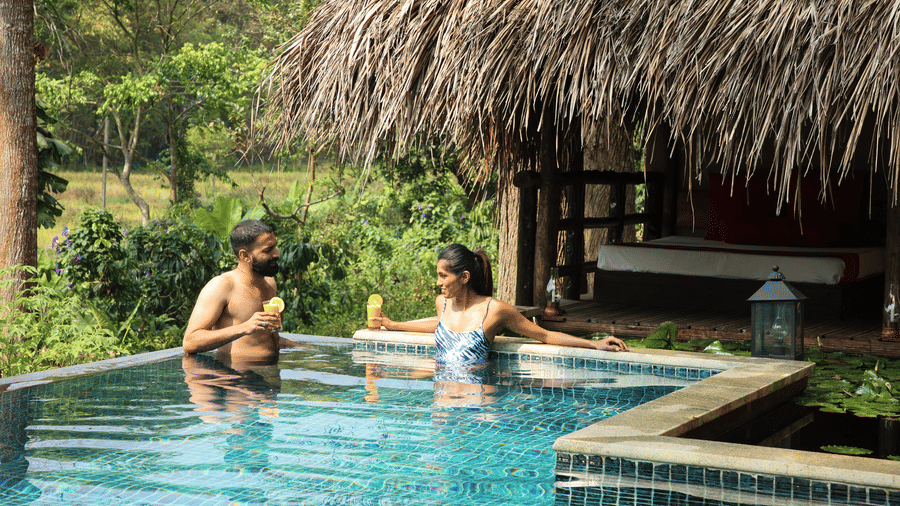 Couple relaxing in a private infinity pool with thatched roof villa at Evolve Back Coorg
