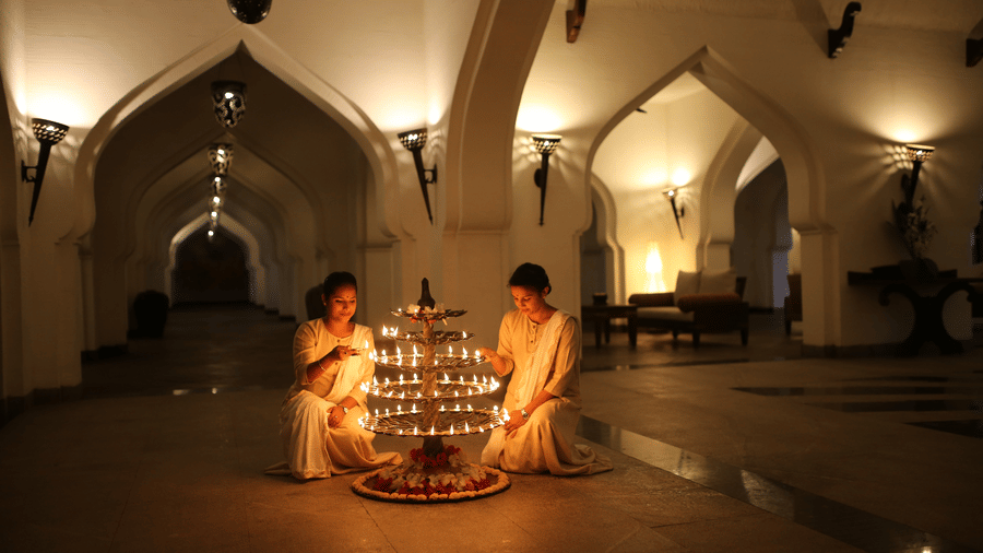 Guests participating in a diya lighting ceremony in an arched corridor at Evolve Back Hampi