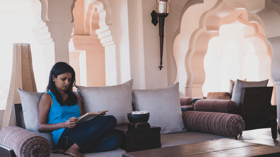 Guest relaxing and reading in a lounge suite with arched architecture at Evolve Back Hampi
