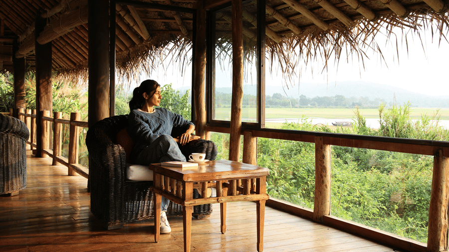 Guest relaxing on a thatched riverside deck overlooking paddy fields at Evolve Back Kabini