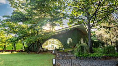 A low building at Amanzi Resort with a large arched entrance is viewed from a stone path across a manicured green lawn at sunset.