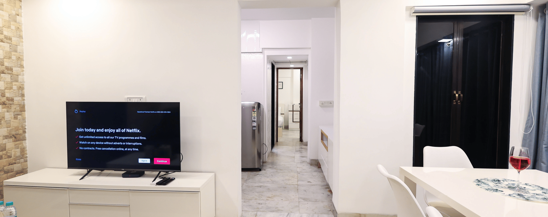 Open plan living area at Wabi-Sabi, Juhu with a TV unit, a stone accent wall, a dining table, and a corridor leading to the kitchen.