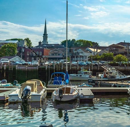 Small boats docked at a harbour with buildings and trees in the background.