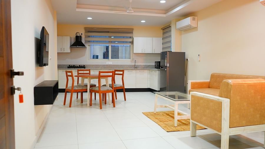 A spacious hall features a sofa, dining table and chairs, a TV and a kitchen - A M Suites
