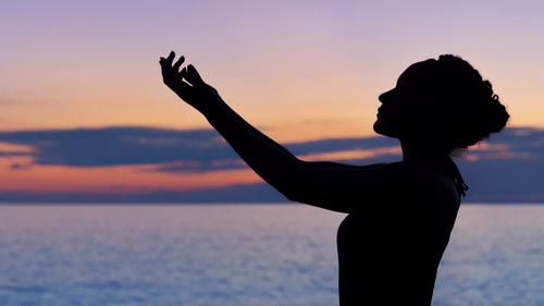 silhouette of woman doing yoga by the beach