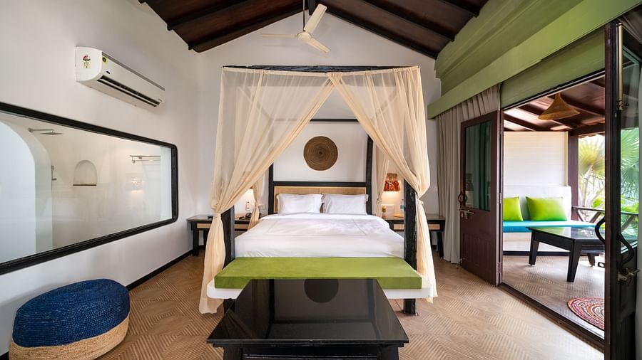 Elegant bedroom with a canopy bed, vibrant green accents, artistic wall decor, and a seating area opening to a private patio with outdoor seating