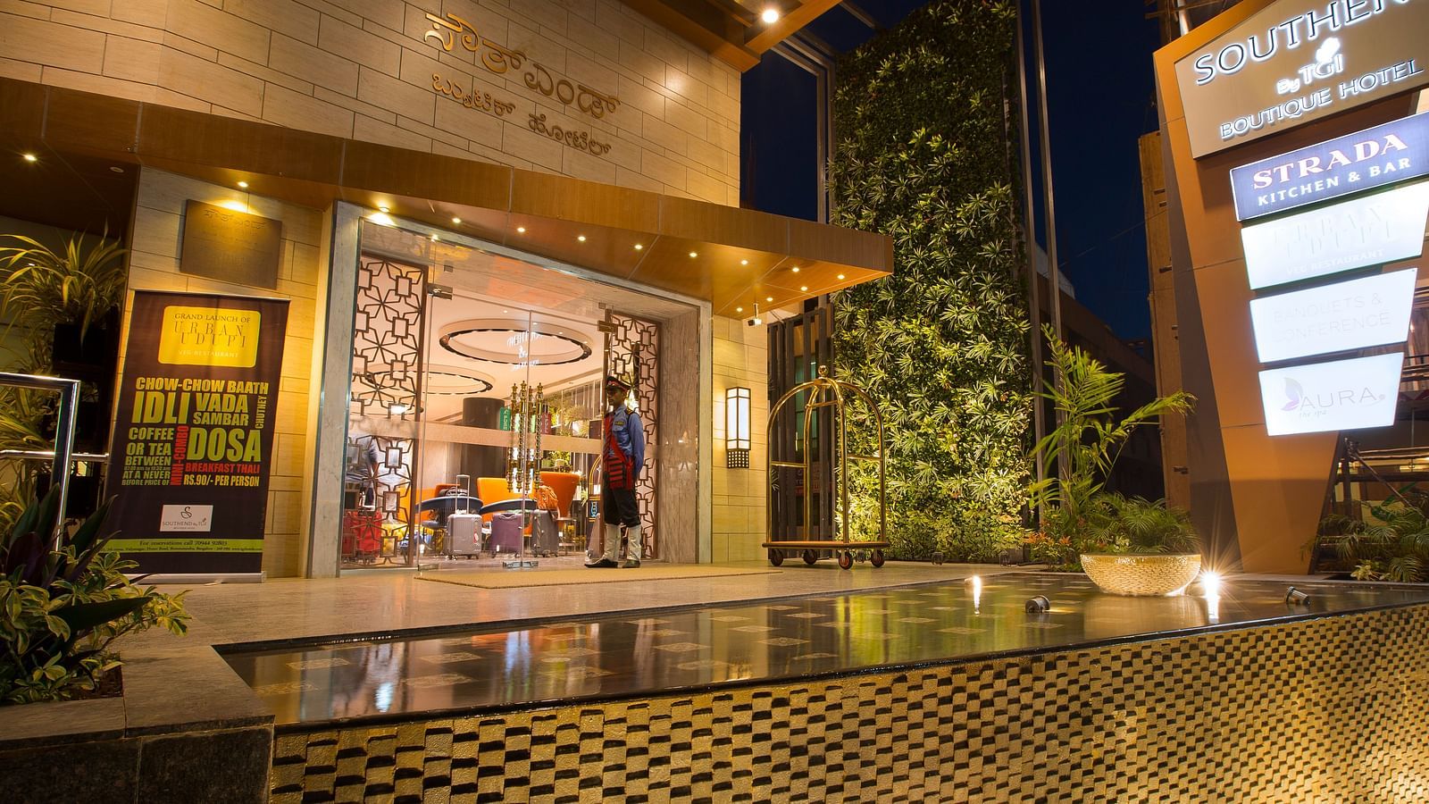 The exterior entrance of a hotel at dusk, featuring signage, a bellhop and a reflective water feature - Hotel Southend by TGI - Bommasandra, Bangalore