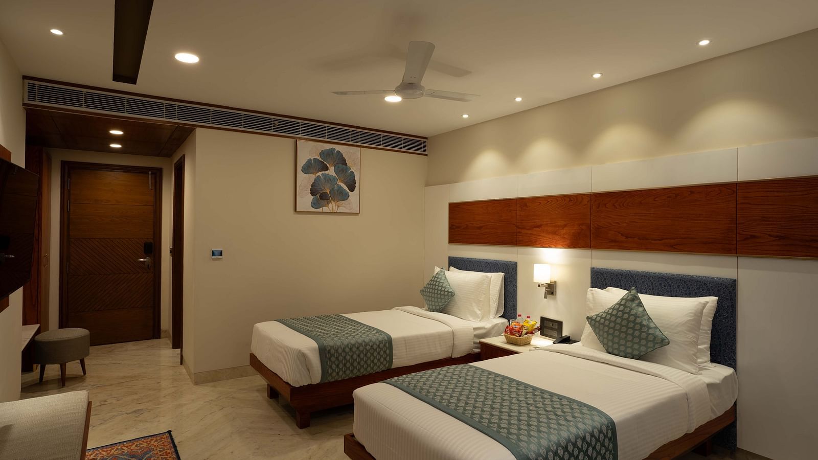 Deluxe Room with twin beds along with a wooden side table with a lamp and wooden table and chair at Inde Signature Jaipur