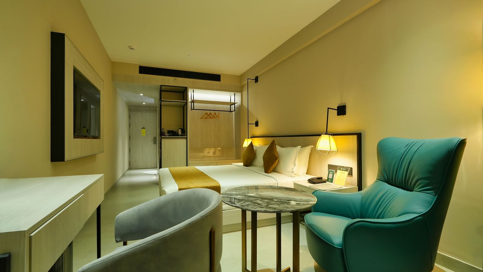 Hotel room at Mesta Hotel showing seating area with teal chair, round table, and contemporary lighting with large windows.