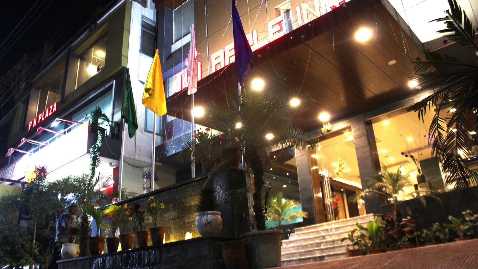 A low angle shot of the hotel at night illuminated by yellow and white lights and flags placed at the front - TGI Apple Inn, Jaipur 