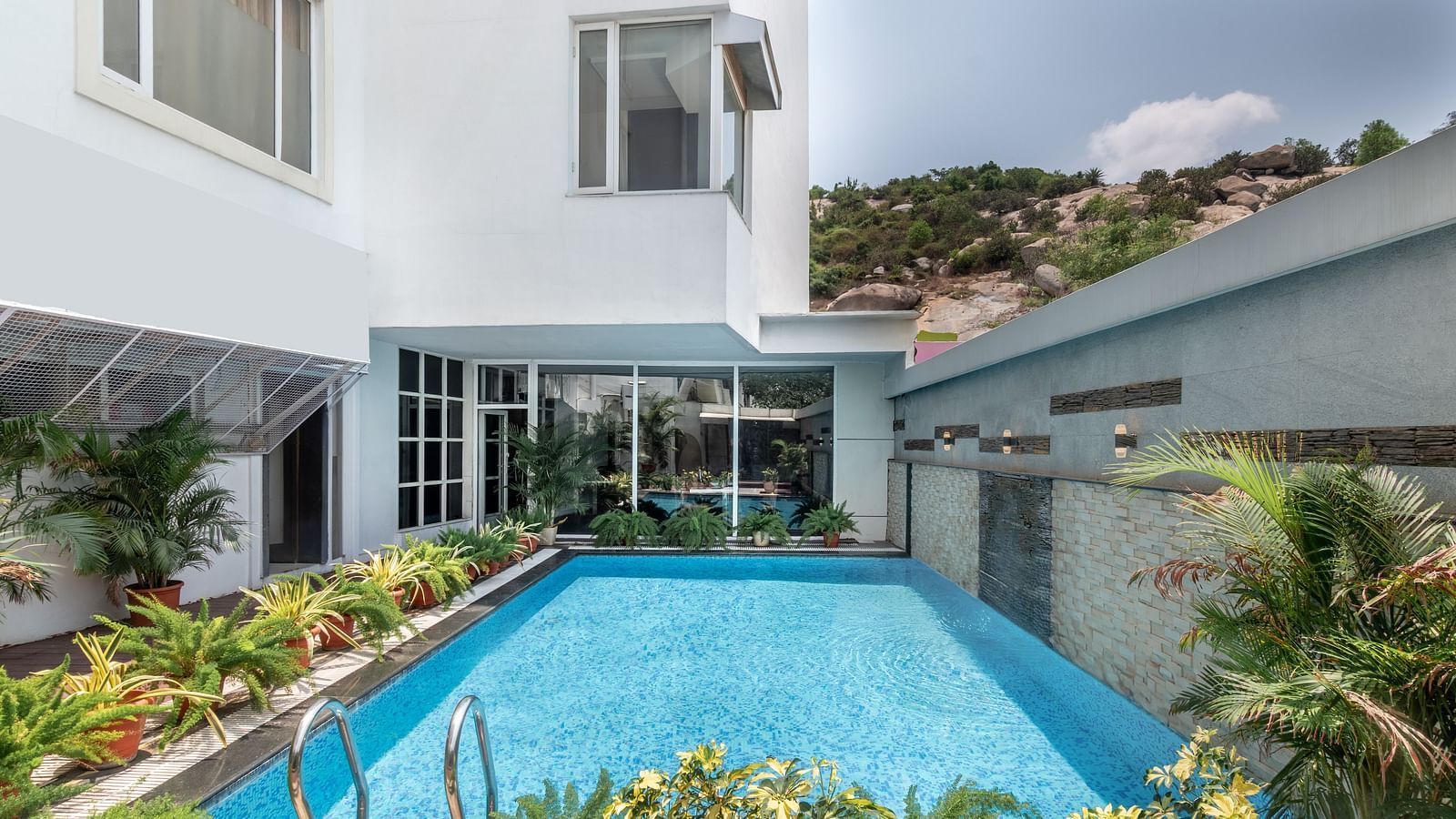 A swimming pool with clear water is surrounded by landscaping and a white building. The sky is overcast.