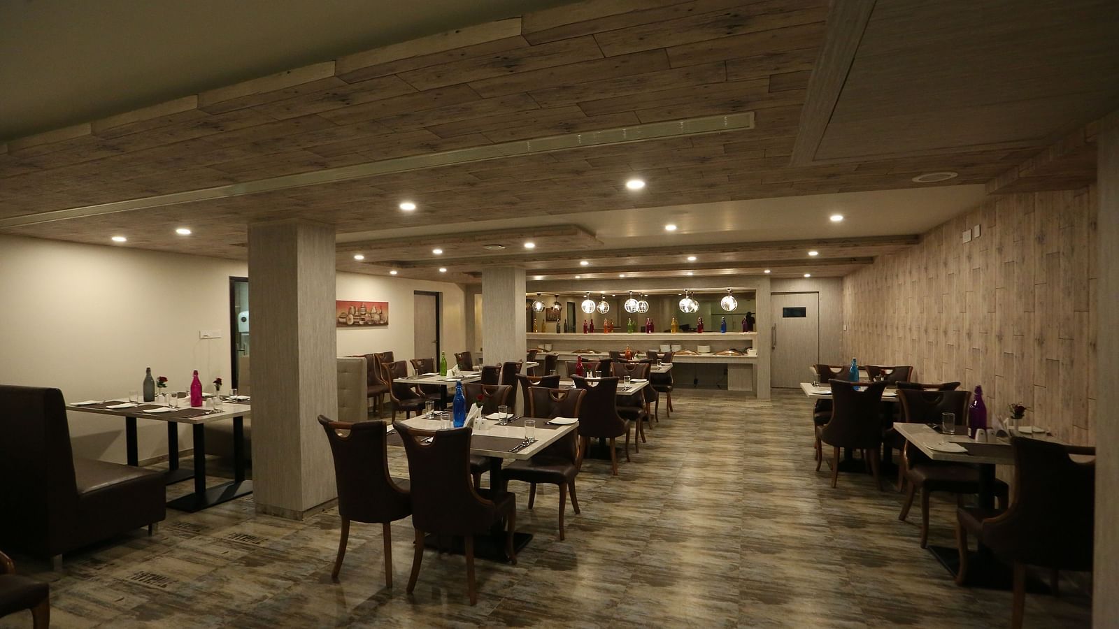 A long, spacious restaurant with tables and chairs, illuminated by ceiling lights - TGI SPS Grand, Coimbatore