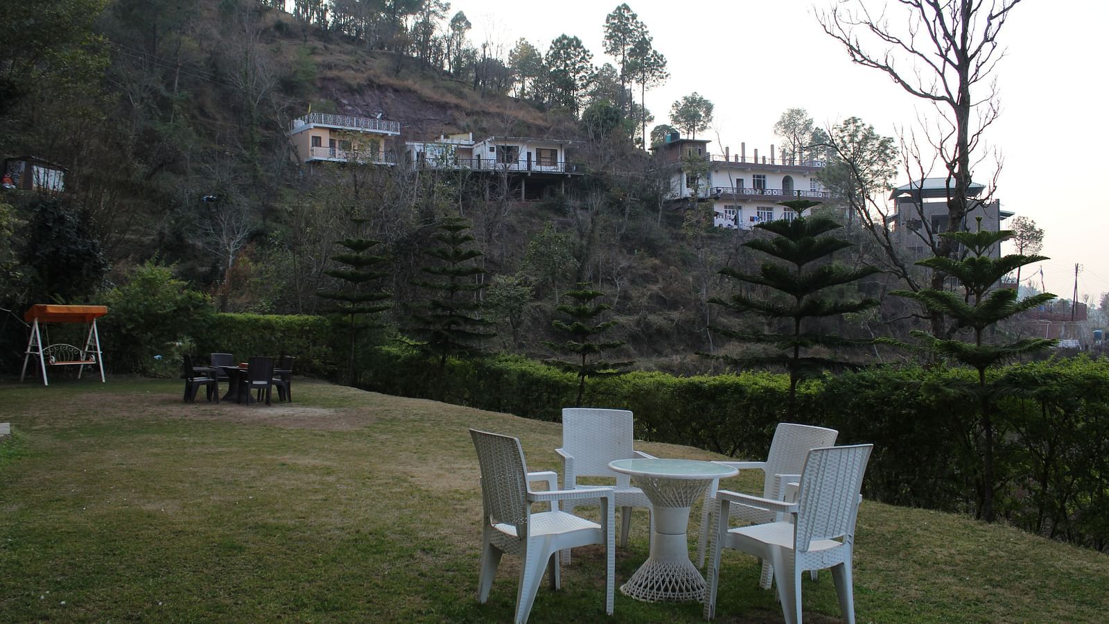 A beautifully maintained garden space with outdoor seating and a backdrop of hill slopes and trees at Dagshai Manor Kasauli - Inde Hotels.