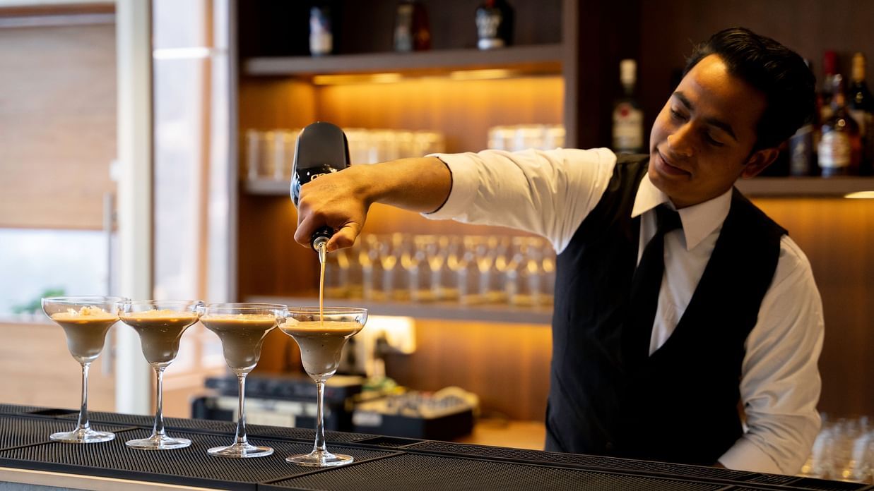 A bartender prepares drinks at a bar with bottles and glasses.