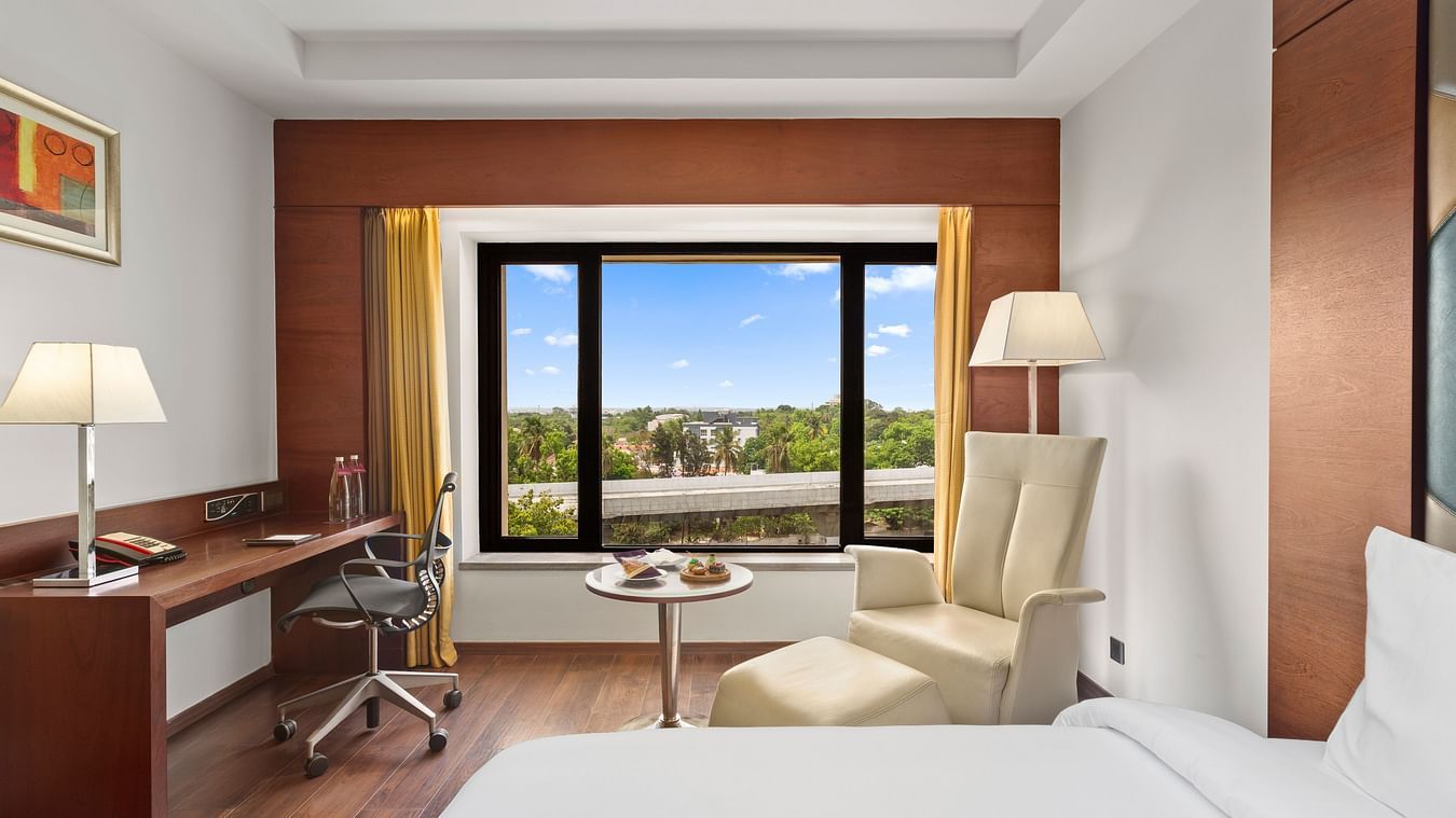 Spacious bedroom with a cozy chair, corner lamp, and a city view from the window at The Residency Towers Coimbatore