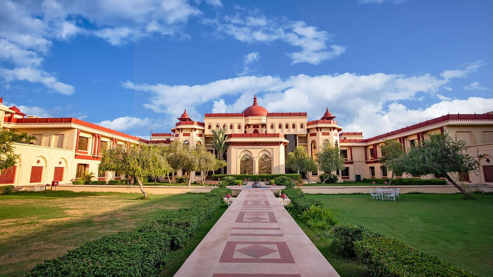 Grand exterior view of The Ummed Jodhpur Palace Resort & Spa with a wide pathway, lush green lawns, and clear blue sky.
