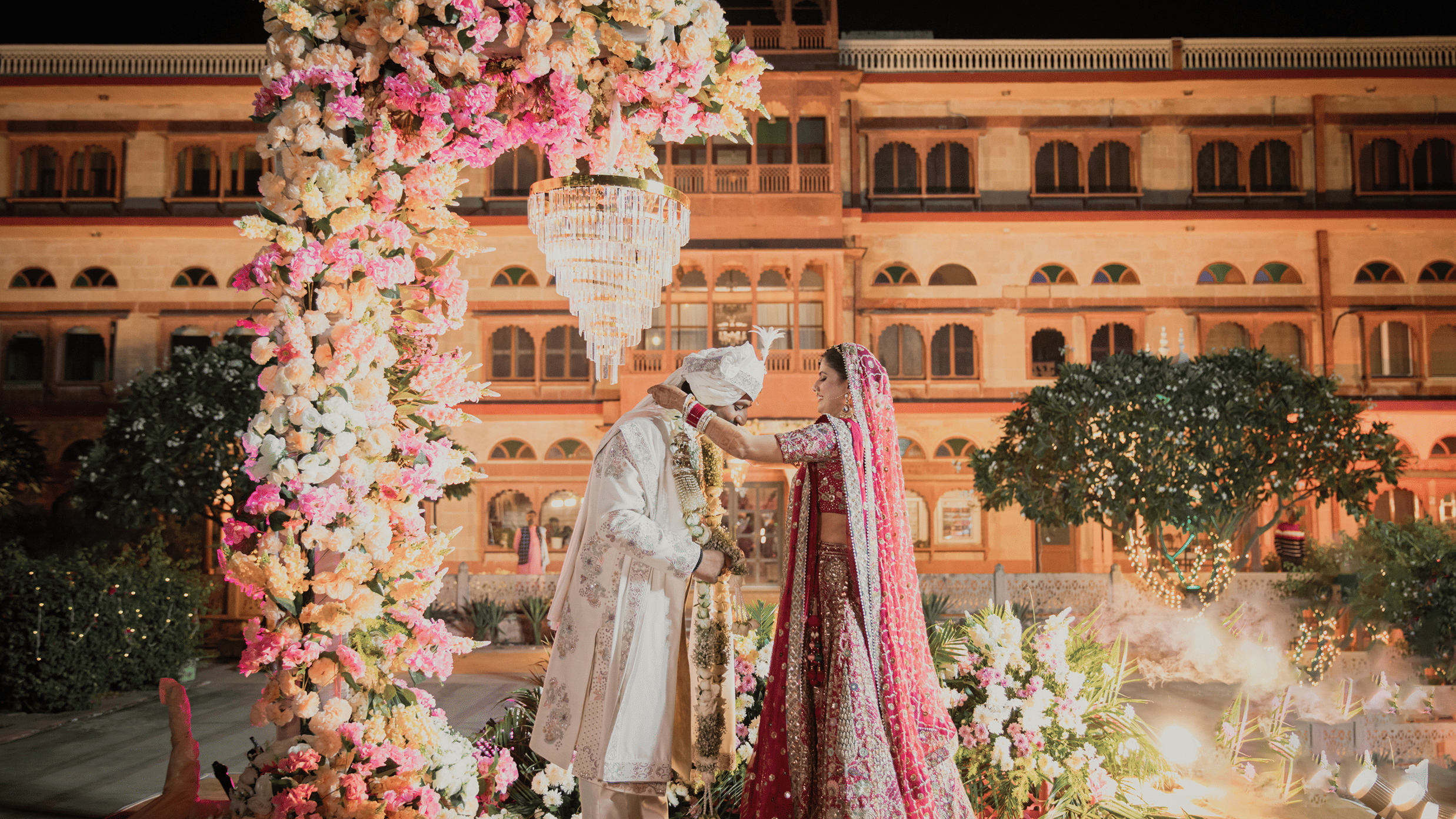 A couple in their wedding attire standing at the wedding alter with Umaid Palace, a royal wedding palace venue as their background.