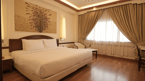 A well-lit bedroom with a king size bed, wooden flooring, curtains, and a seating area, reflecting comfortable rooms in Jaipur - Clarks Amer, Jaipur