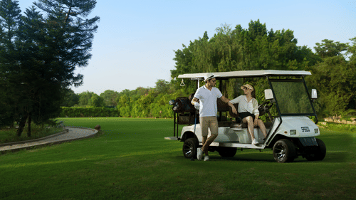 2 guests chatting with each other as they are placed on the golf cart, surrounded by a lush green lawn and trees at Heritage Village Resorts & Spa, Manesar, perfect for a luxury staycation near Gurgaon.