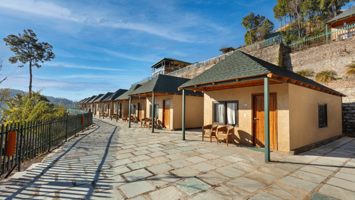 An image of cottage rooms from outside featuring a concrete yard at front and the entire villa is surrounded by trees in the hills - Suryavillas Luxury Resort and Spa, Solan