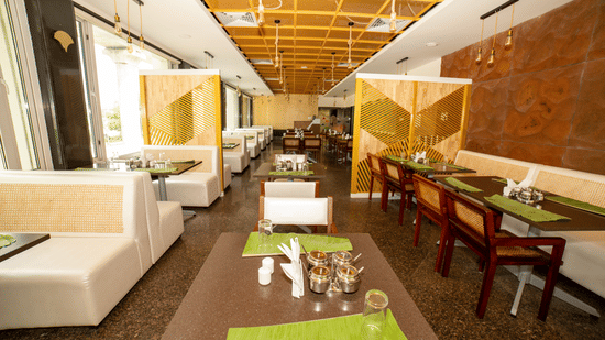 Close-up of comfortable white booth seating and adjacent dining tables with green placemats in Icon Express By Bhagini, Mahadevapura.
