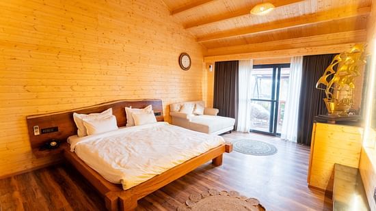 Cozy wooden bedroom with a double bed, sofa, warm lighting, and large windows opening to a balcony at Themis Farm House.
