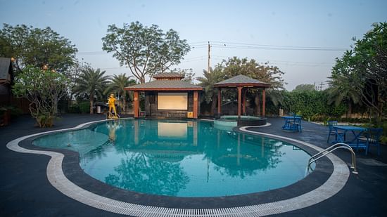 A tranquil swimming pool at Themis Farm House is surrounded by lush greenery and relaxation areas under a clear evening sky.